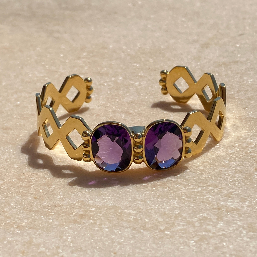 Gold earrings with purple gemstones on a textured beige background