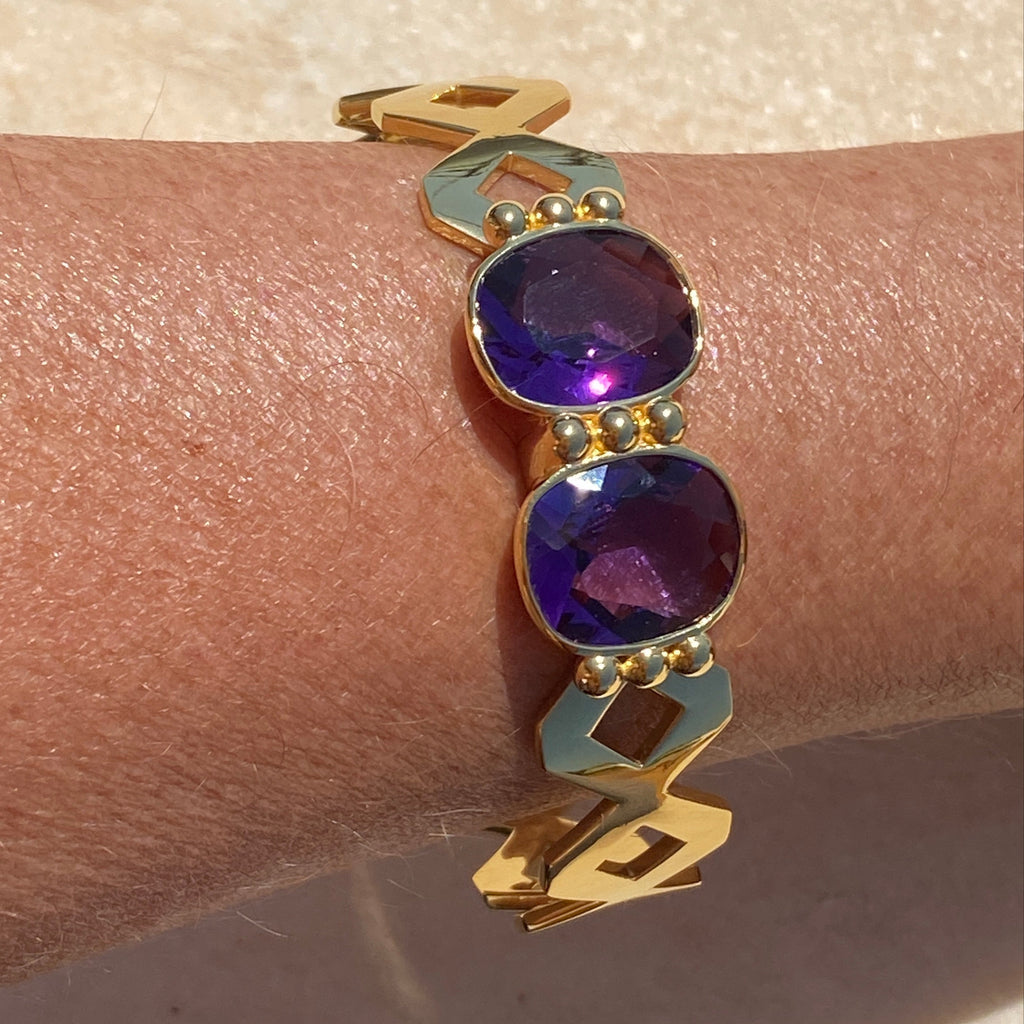 Gold bracelet with purple stones on a wrist against a light background