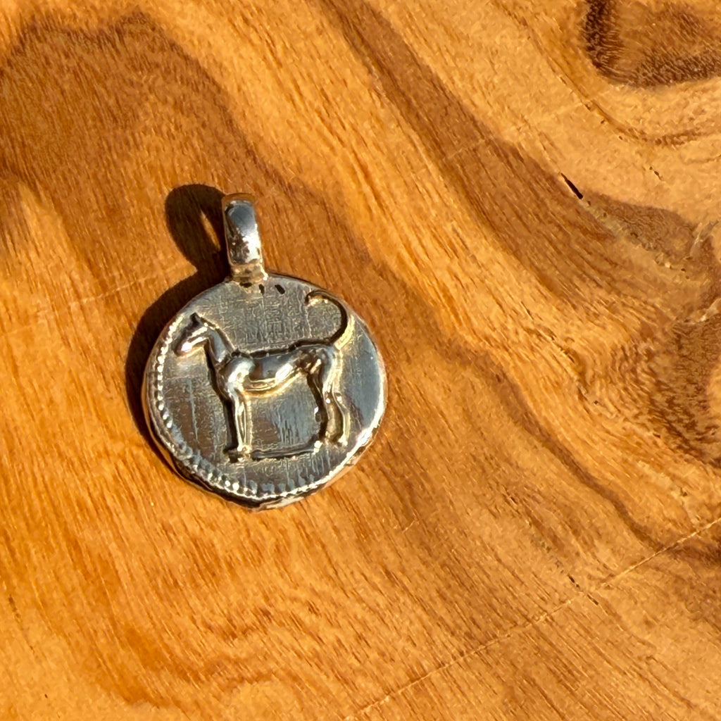 Silver pendant with a dog design on a wooden surface