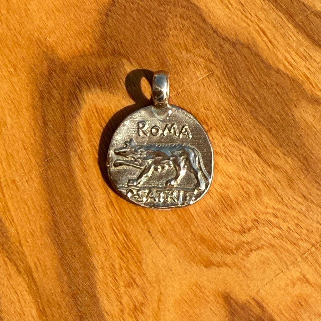 Silver pendant with 'Roma' engraving on a wooden surface