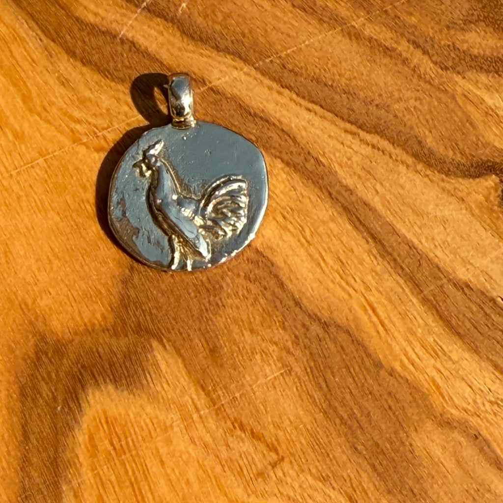 Silver rooster pendant on a wooden surface