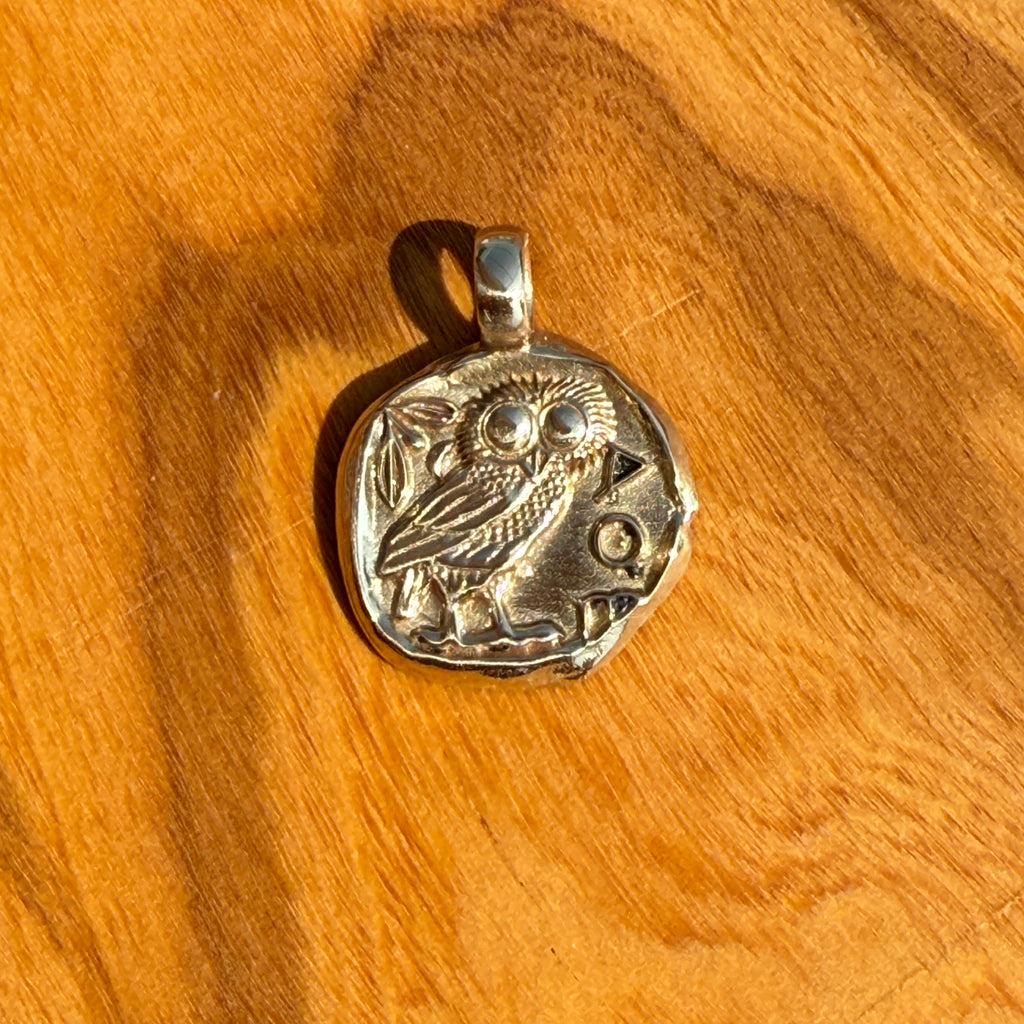 Silver pendant with owl design on a wooden surface