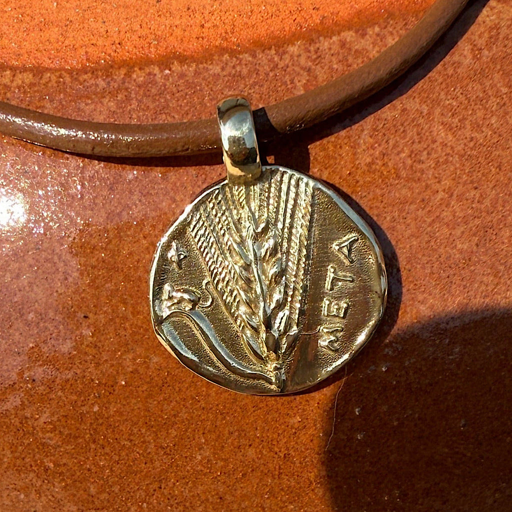 Gold pendant with engraved design on a brown leather cord against an orange background
