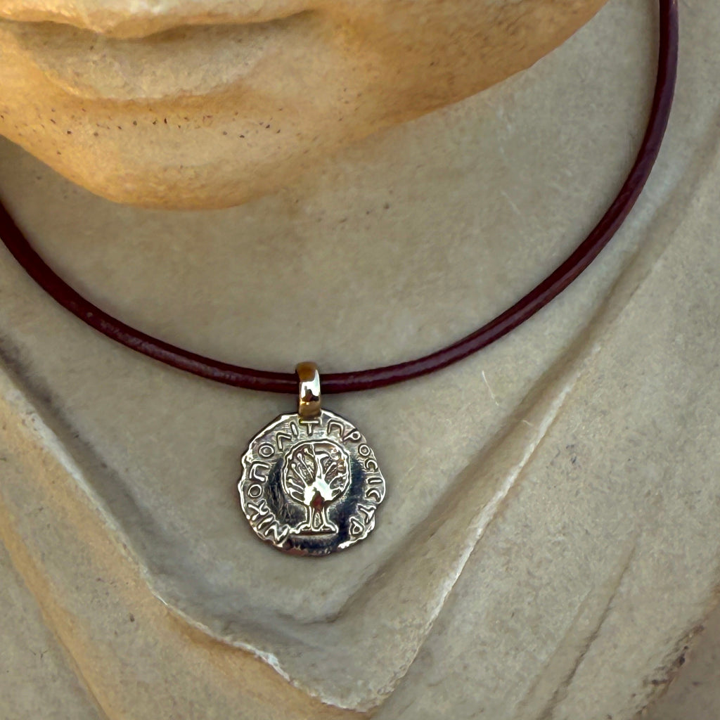 Silver pendant on a red cord worn by a stone bust