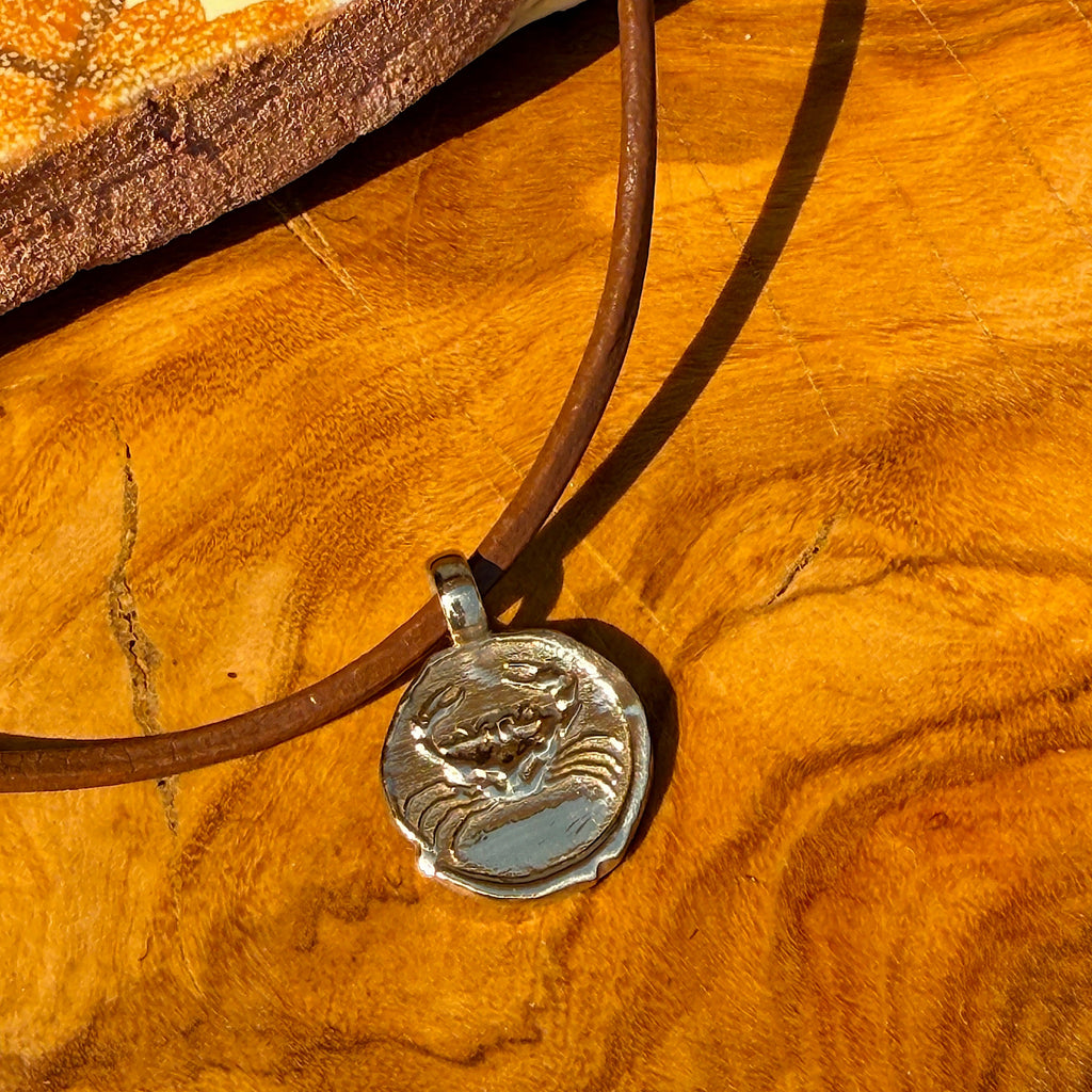 Silver pendant on a brown cord against a wooden background